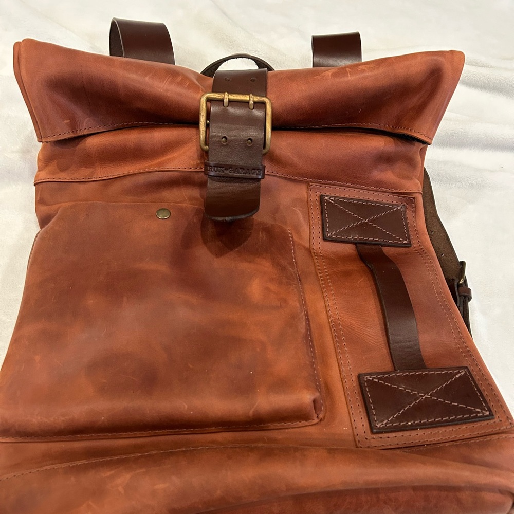 Cognac brown roll top leather backpack with short buckle strap closure.